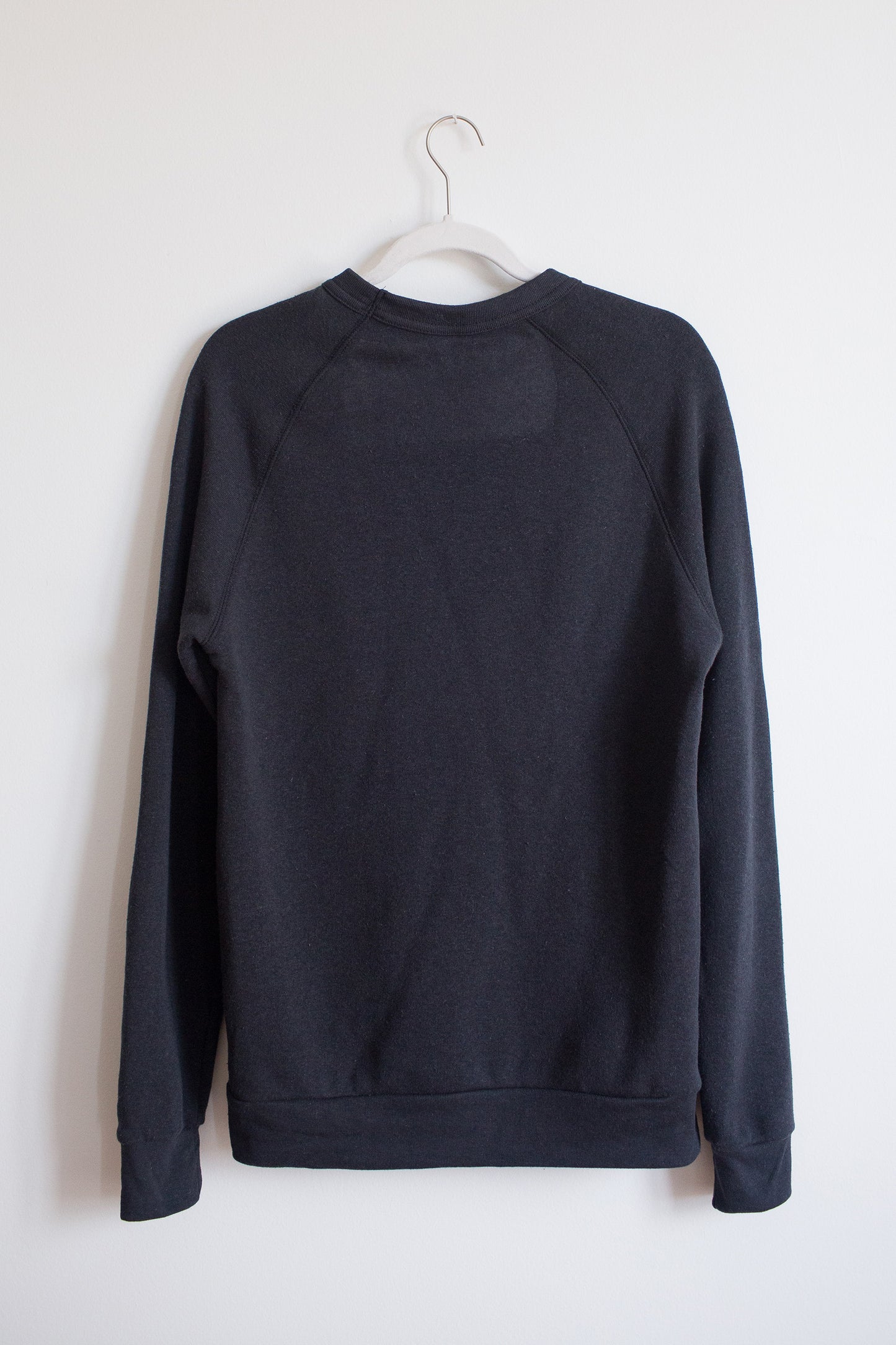 Hanging back of black crewneck sweatshirt with raglan sleeves.